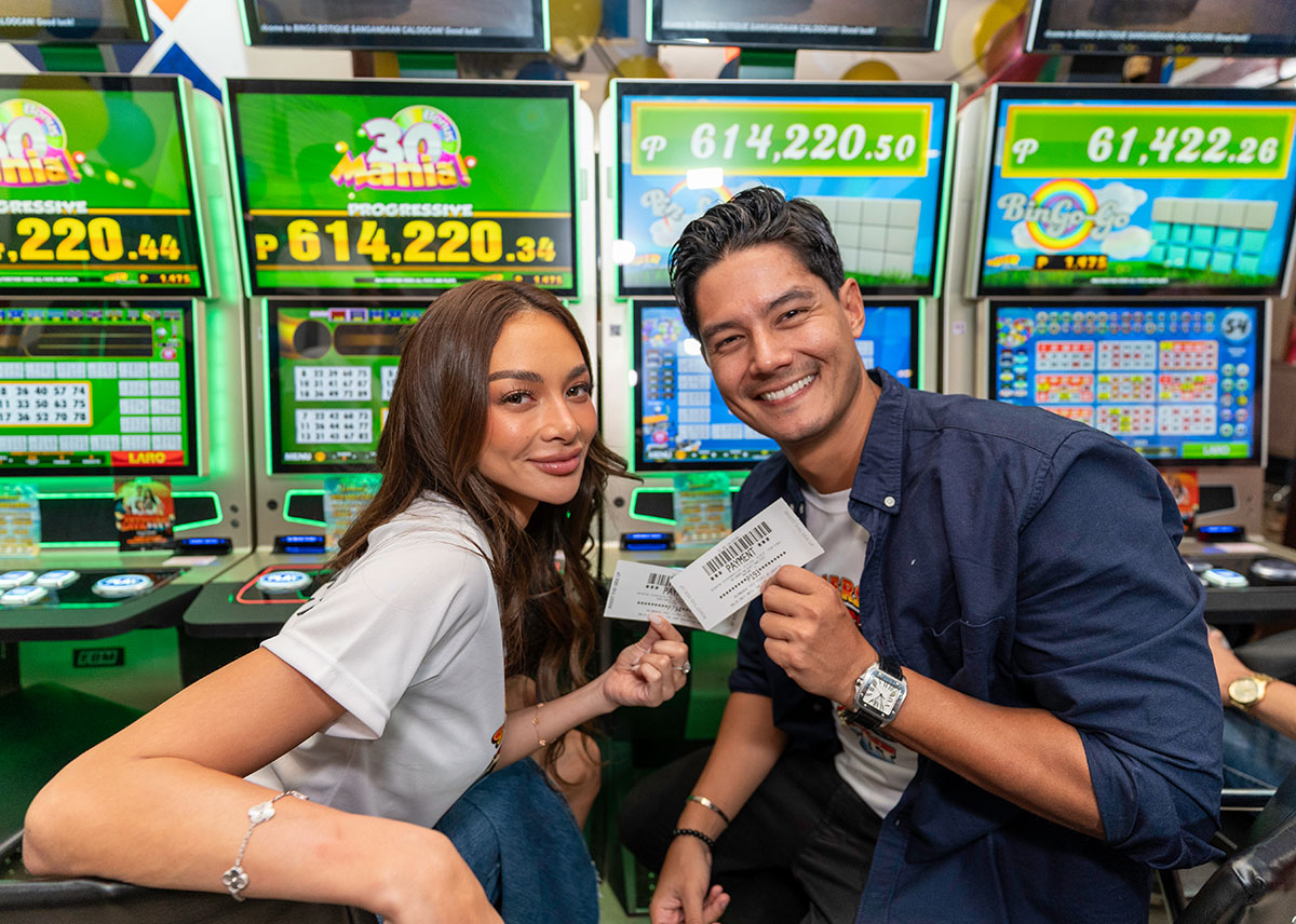 La imagen muestra a Kylie Verzosa y Daniel Matsunaga sosteniendo boletos frente a gabinetes de casino que ejecutan video bingos de FBM en la iniciativa Summersaya Fest.