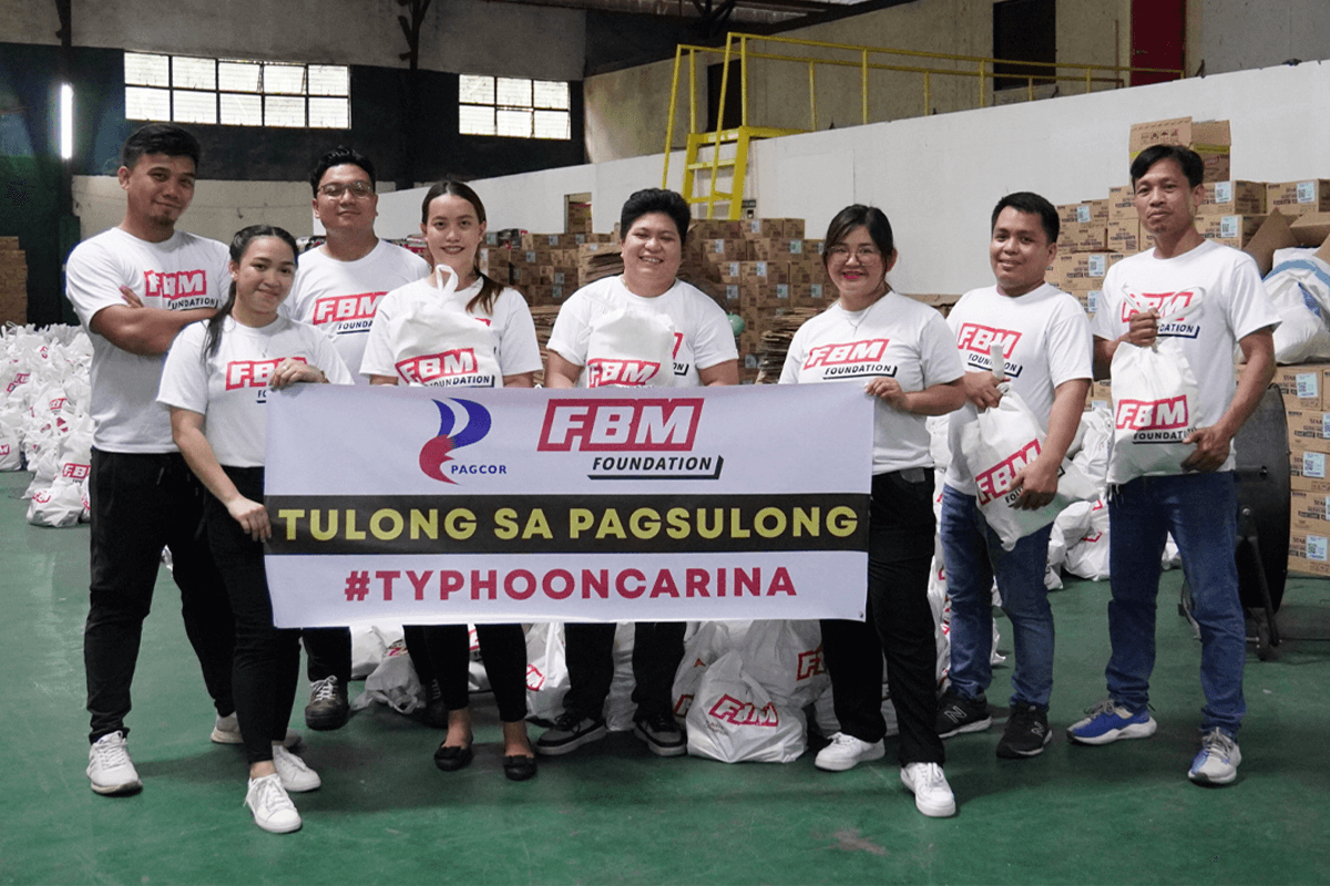 The image shows FBM Foundation volunteers holding a banner during the donation of relief kits for the victims of Typhoon Carina in the Philippines.