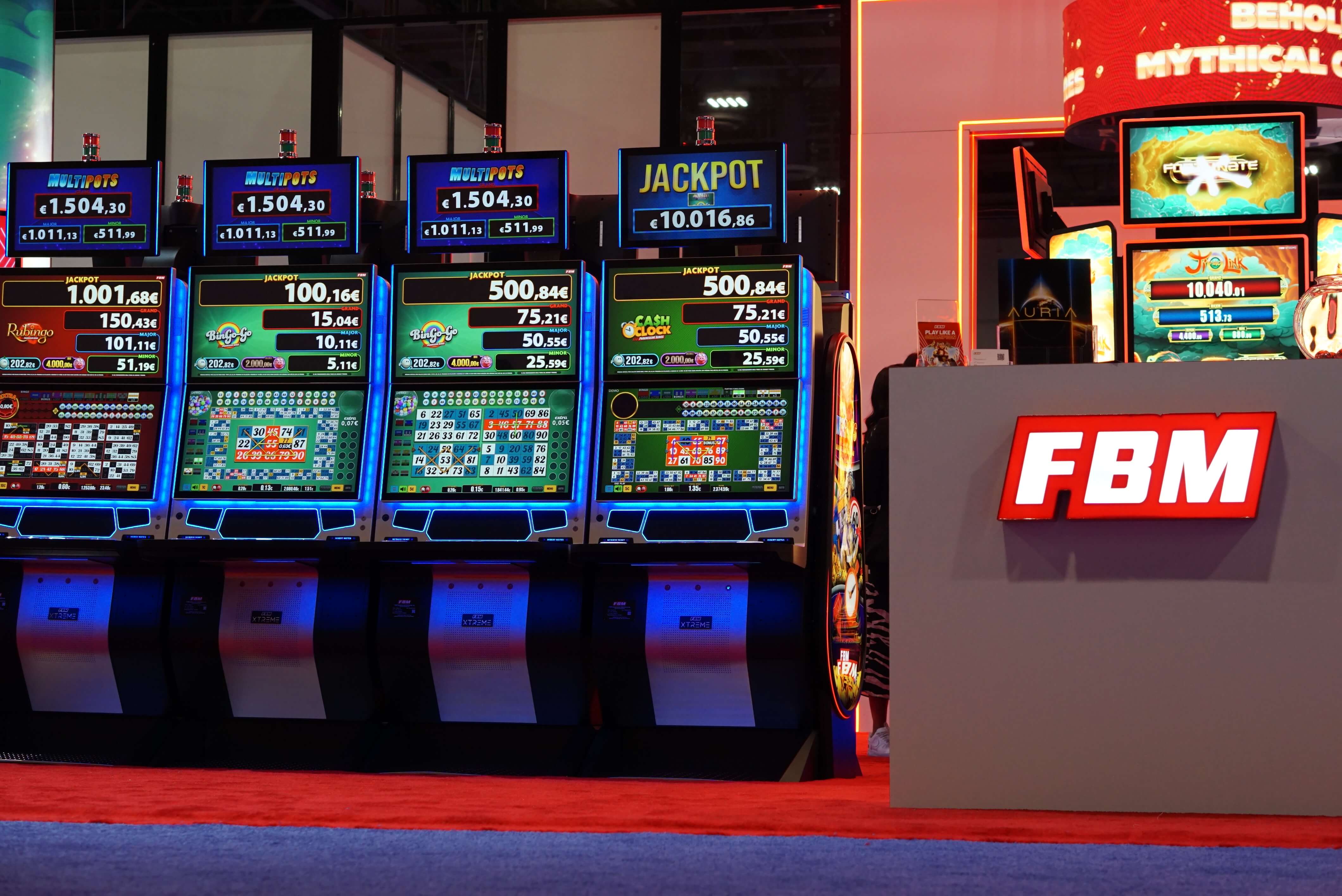 Esta imagen muestra cuatro gabinetes de casino FBM exhibiendo juegos de video bingo en una feria comercial internacional.