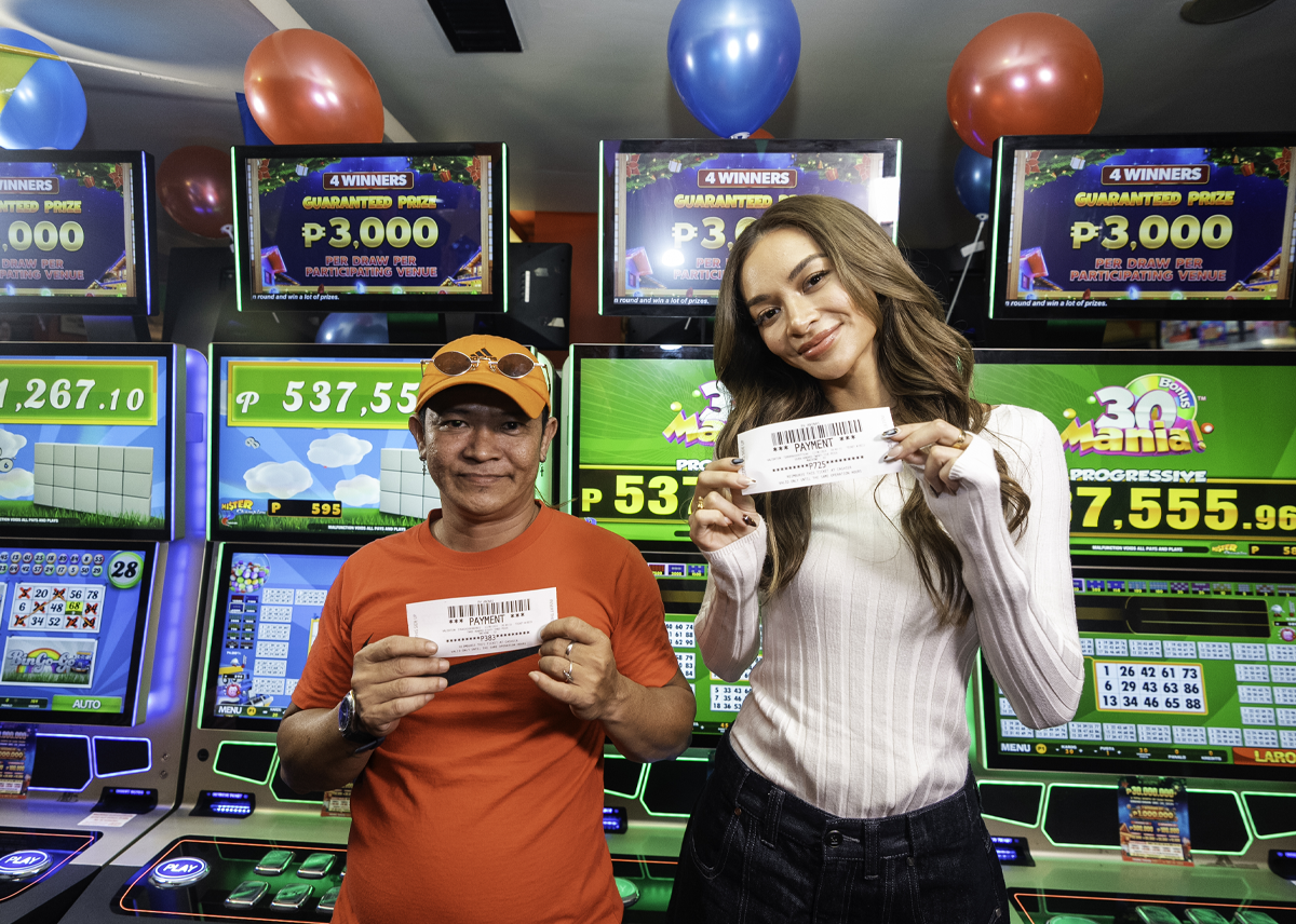 The image shows an FBM video bingo player with Kylie Verzosa in front of the brand casino cabinets after winning a prize playing one of the FBM video bingos.