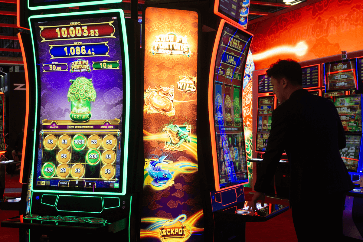 Esta imagen muestra a un visitante en el stand de FBM en G2E Las Vegas probando el slot Xing Fú Fortune Money Trees.
