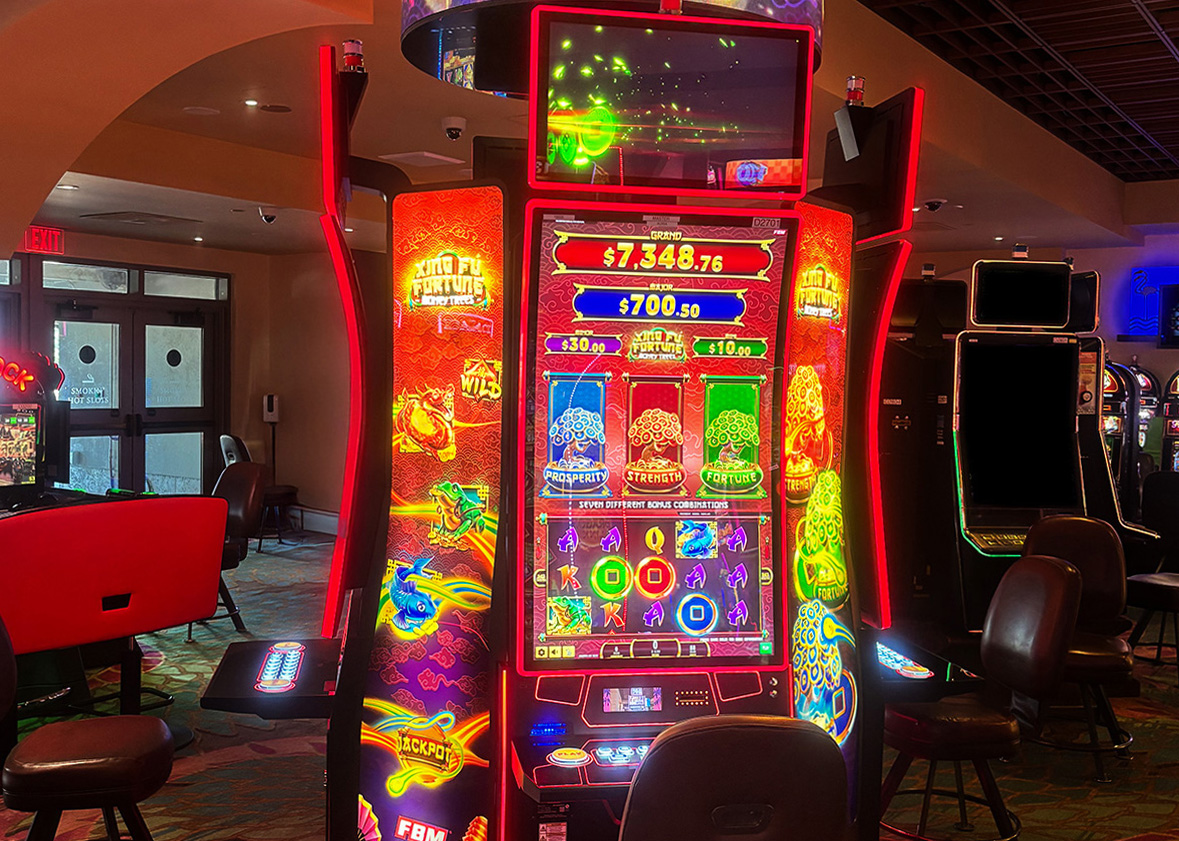 La imagen muestra los gabinetes de casino Auria de FBM con el slot Xing Fú Fortune Money Trees instalado en el piso del casino Hialeah Park.