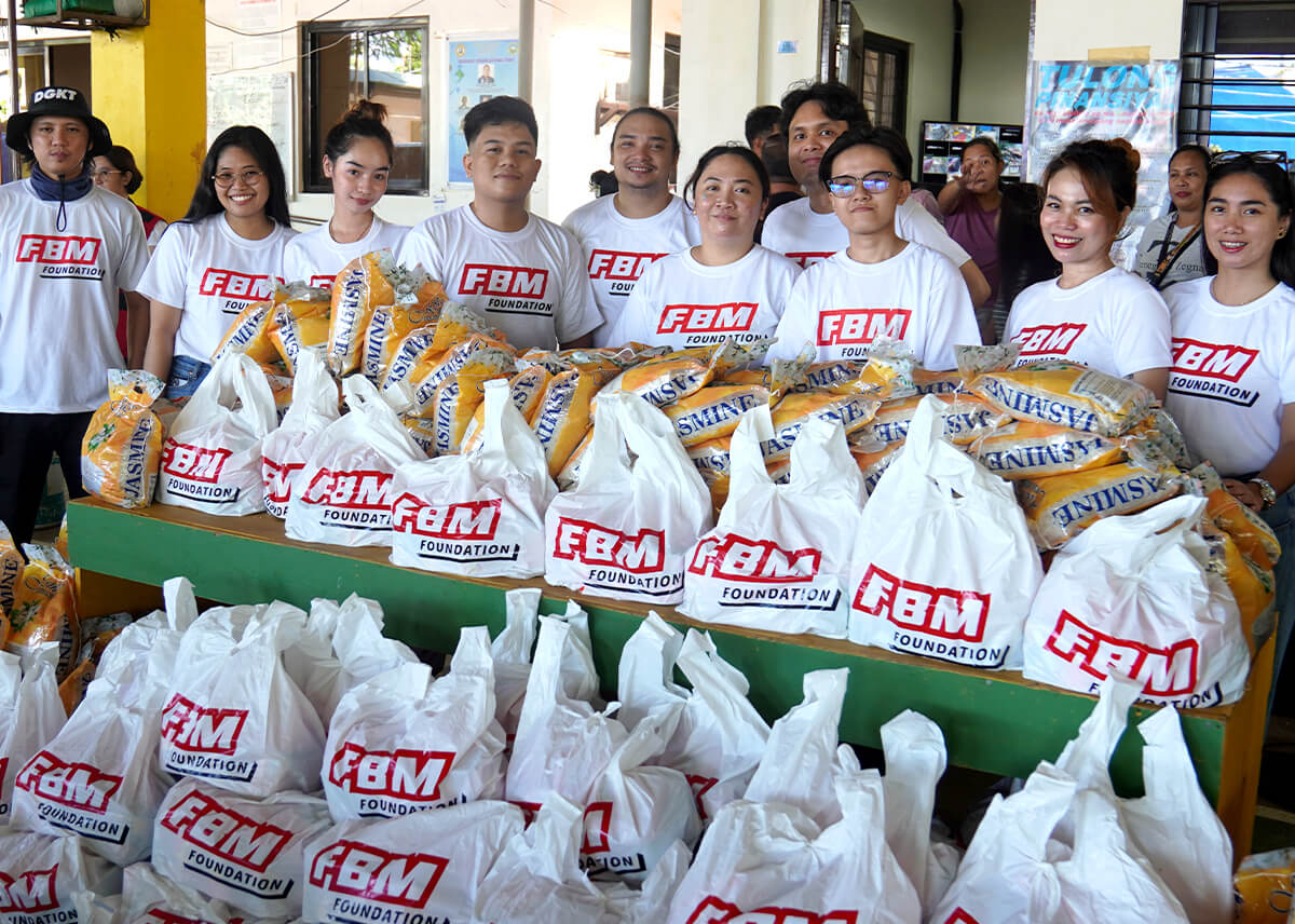 A group of FBM Foundation volunteers proudly stands behind a table filled with relief goods, ready to be distributed to families in need.
